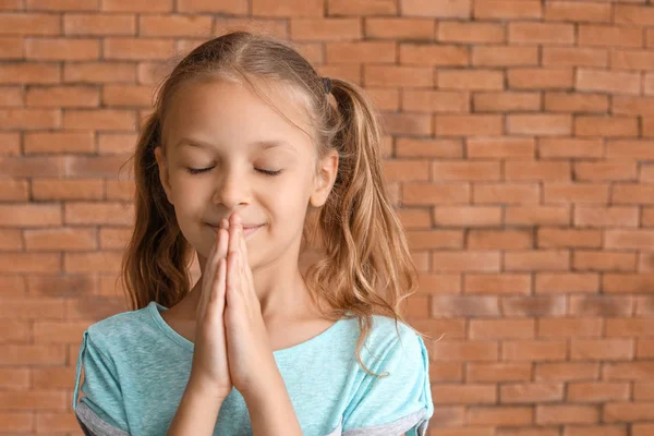 Cute little girl praying against brick wall — Stock Photo, Image