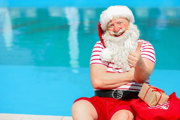 Papai Noel com presentes mostrando polegar-up perto da piscina no resort — Fotografia de Stock