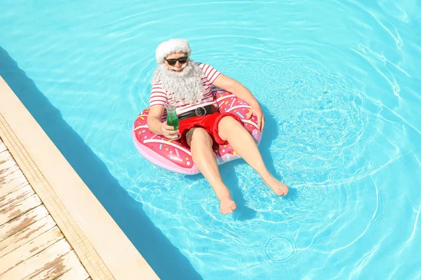 Santa Claus relaxing on inflatable ring in swimming pool — Stock Photo, Image