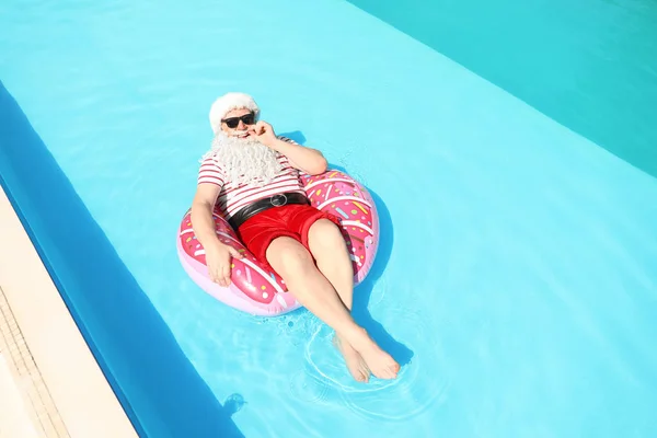 Santa Claus relaxing on inflatable ring in swimming pool — Stock Photo, Image