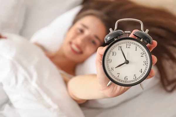 Morning of beautiful young woman with alarm clock in bed — Stock Photo, Image