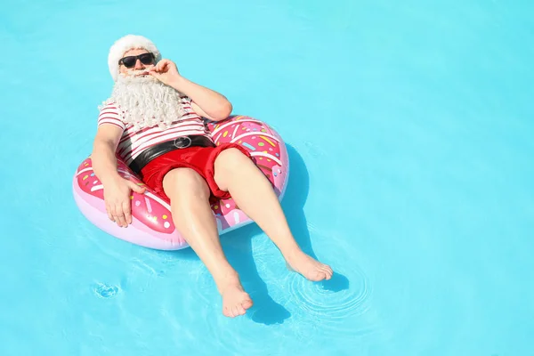 Santa Claus relaxing on inflatable ring in swimming pool — Stock Photo, Image