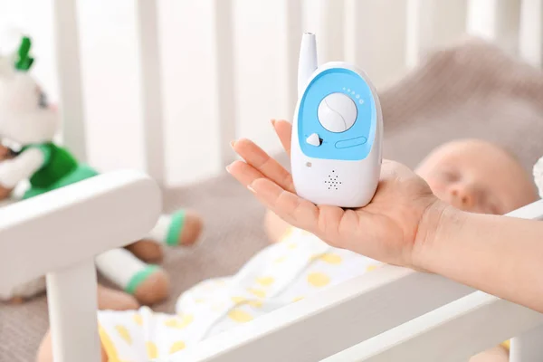 Female hand with modern baby monitor and little sleeping child on background — Stock Photo, Image