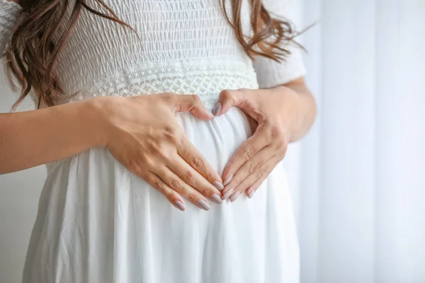 Giovane donna incinta che fa cuore con le mani, primo piano — Foto Stock