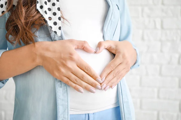 Молода вагітна жінка робить серце руками на білому тлі, крупним планом — стокове фото