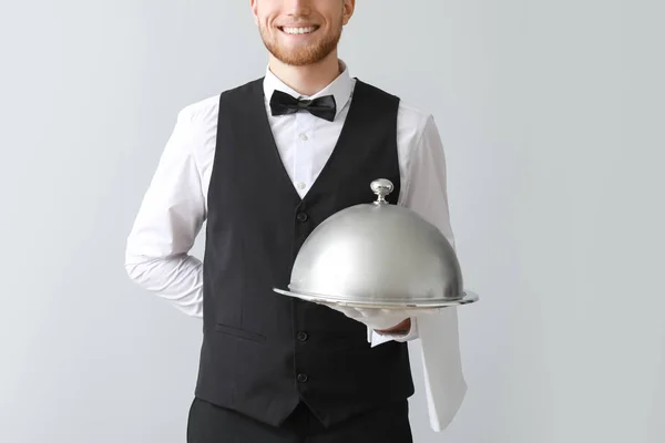 Bellissimo cameriere con vassoio e cloche su sfondo chiaro — Foto Stock