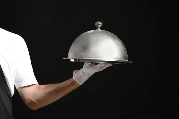 Hand of waiter with tray and cloche on dark background — Stock Photo, Image