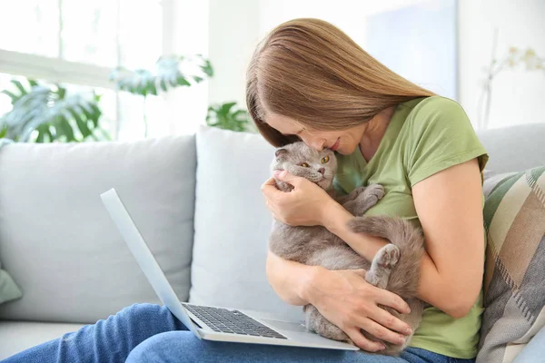 Beautiful woman with cute cat and laptop sitting on sofa at home — Stock Photo, Image