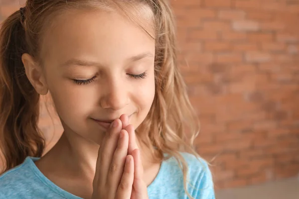 Cute little girl praying against brick wall — Stock Photo, Image