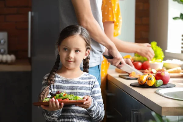 Menina com pais preparando salada de legumes na cozinha — Fotografia de Stock