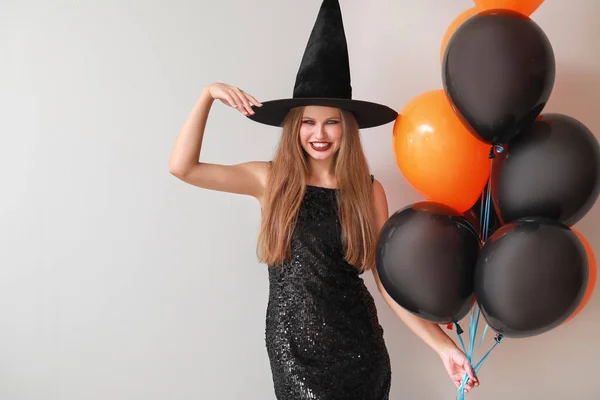 Krásná žena oblečená jako čarodějnice na Halloween na světlém pozadí — Stock fotografie