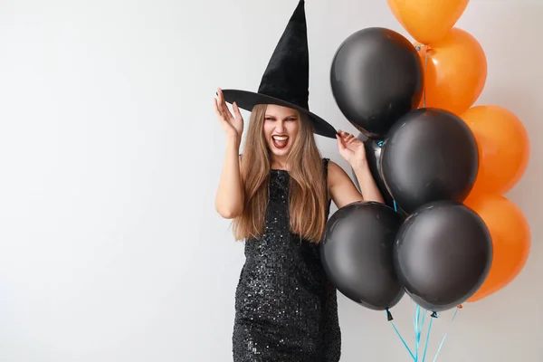 Piękna kobieta, ubrana jak czarownica Halloween na jasnym tle — Zdjęcie stockowe