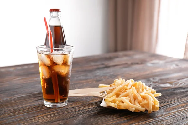 Cola fría y sabrosas papas fritas sobre mesa de madera — Foto de Stock