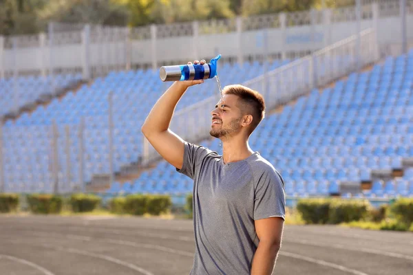 Handsome sporty man refreshing himself with water after training outdoors