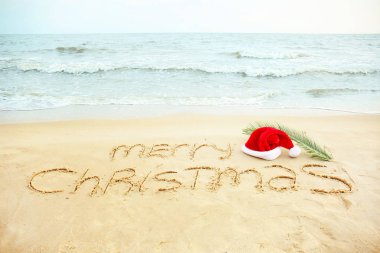 Deniz kıyısında yazılı metin Merry Christmas ile Noel Baba şapka. Noel tatili