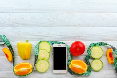 Ahşap arka planda taze meyve, sebze ve ölçüm bandı ile modern cep telefonu