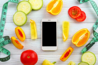 Ahşap arka planda taze meyve, sebze ve ölçüm bandı ile modern cep telefonu