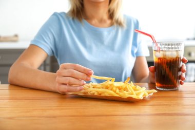 Masada bir bardak soğuk kola ve patates kızartması olan kadın