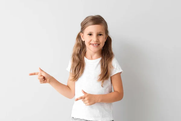 Little girl in stylish t-shirt pointing at something on light background — Stock Photo, Image