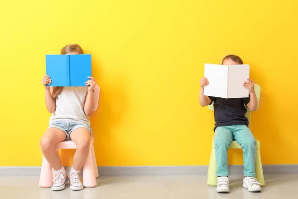 Little children with books sitting on chairs near color wall — Stock Photo, Image