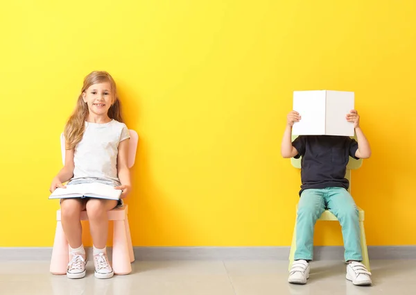Little children with books sitting on chairs near color wall — Stock Photo, Image
