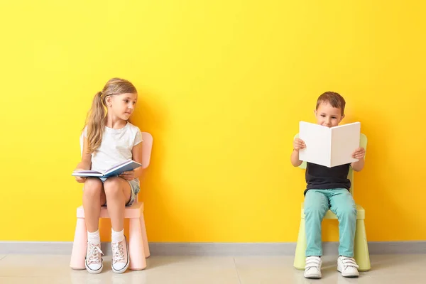 Petits enfants avec des livres assis sur des chaises près du mur de couleur — Photo
