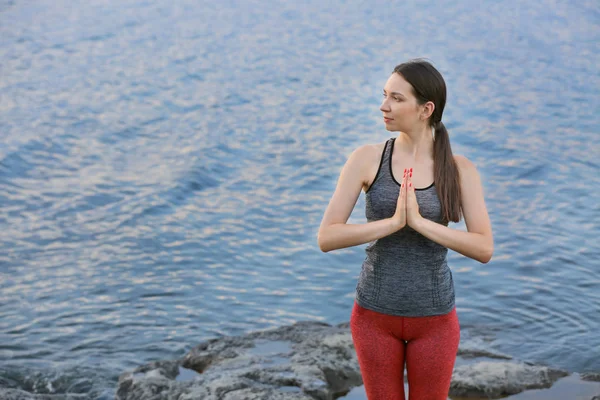 Mujer joven practicando yoga cerca del río —  Fotos de Stock