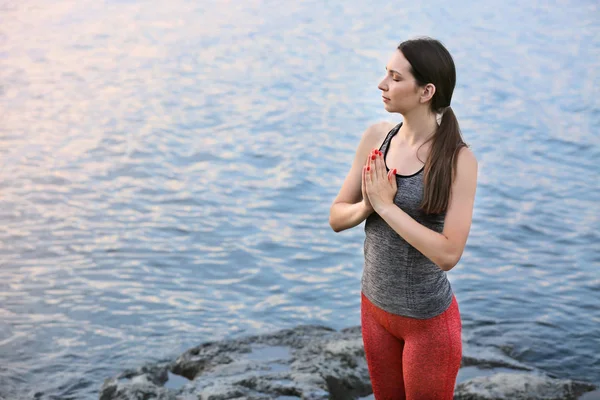 Mujer joven practicando yoga cerca del río —  Fotos de Stock