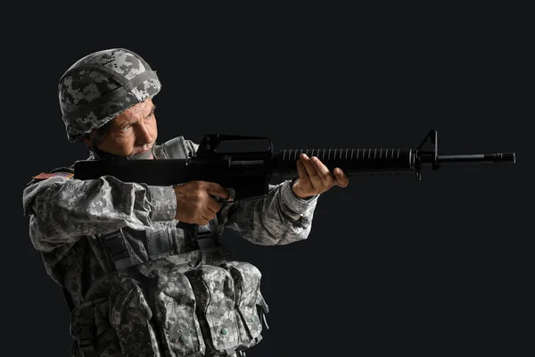 Soldado macho maduro apuntando desde el rifle de asalto sobre fondo oscuro —  Fotos de Stock