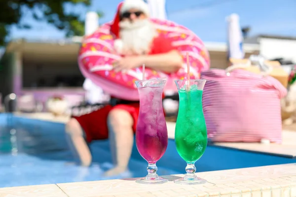 Glasses of cocktails near swimming pool and blurred Santa Claus on background — Stock Photo, Image
