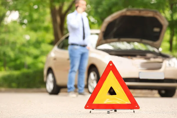 Emergency stop sign and man talking by phone near broken car on road — Stock Photo, Image