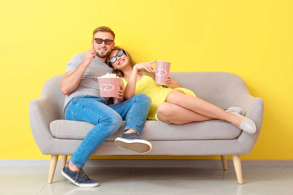 Young couple with popcorn watching movie on sofa near color wall — Stock Photo, Image