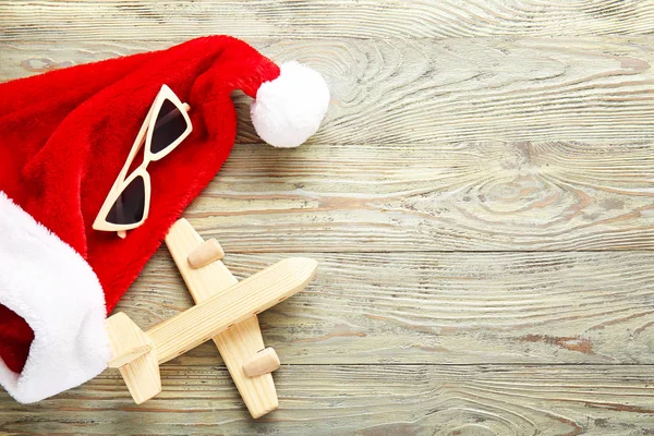 Ahşap arka planda güneş gözlüğü ve uçak ile Noel Baba şapka. Noel tatili — Stok fotoğraf