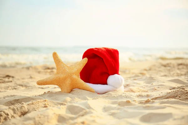 Kapelusz Świętego Mikołaja z rozgwiazdy na wybrzeżu morza. Świąteczne wakacje — Zdjęcie stockowe