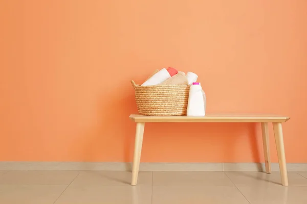 Basket with clean towels and washing agents on table near color wall — Stock Photo, Image