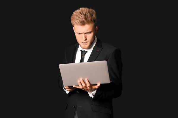 Confused young businessman with laptop on dark background — Stock Photo, Image