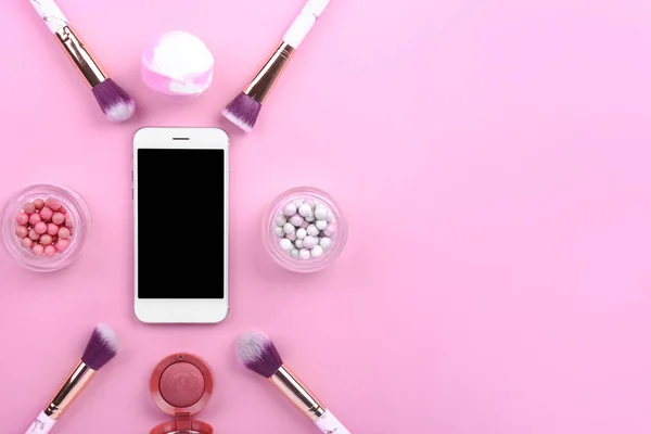 Telefone móvel moderno com pincéis de maquiagem e cosméticos no fundo de cor — Fotografia de Stock