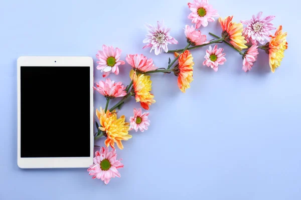 Modern tablet computer with flowers on color background