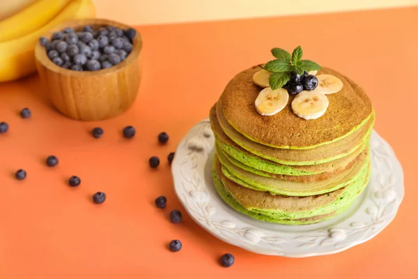 Deilige grønne pannekaker med banan og blåbær på farget bakgrunn – stockfoto