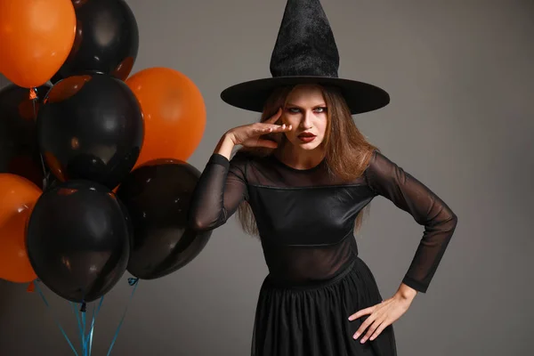 Krásná žena oblečená jako čarodějnice na Halloween na šedém pozadí — Stock fotografie