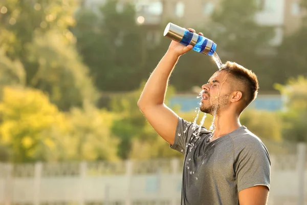 Handsome sporty man refreshing himself with water after training outdoors