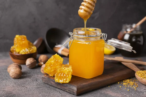 Honey pouring from dipper into jar on table — Stock Photo, Image