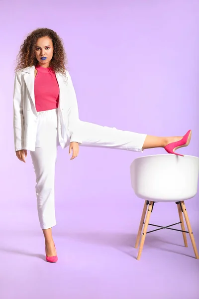 Portrait of fashionable young African-American woman with chair on color background — Stock Photo, Image