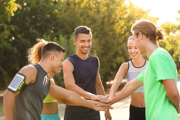 Groep sportieve jonge mensen die de handen in elkaar zetten — Stockfoto