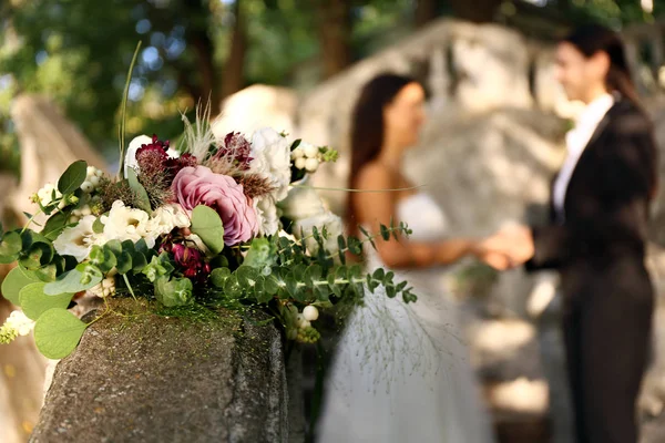 Belo buquê de casamento no corrimão contra casal de lésbicas borradas ao ar livre — Fotografia de Stock