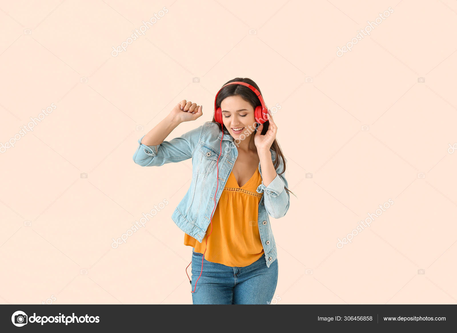 Young woman with headphones dancing against light background Stock