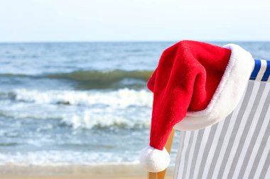 Deniz kıyısında Noel Baba şapkalı plaj sandalyesi. Noel tatili
