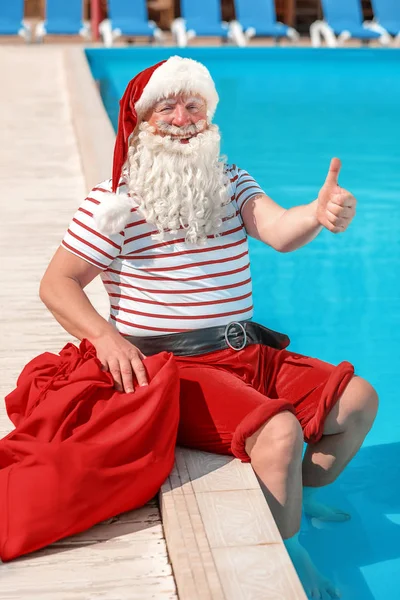 Święty Mikołaj pokazując kciuk w górę w pobliżu basenu w ośrodku — Zdjęcie stockowe