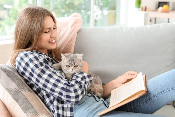 Kaunis nuori nainen söpö kissa käsittelyssä kirja kotona — kuvapankkivalokuva