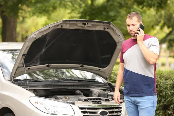 Hombre llamando a su agente de seguros mientras está de pie cerca de coche roto en la carretera — Foto de Stock